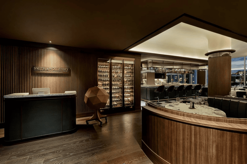 Dimly lit restaurant interior with a curved wooden counter, wine display, and bar seating